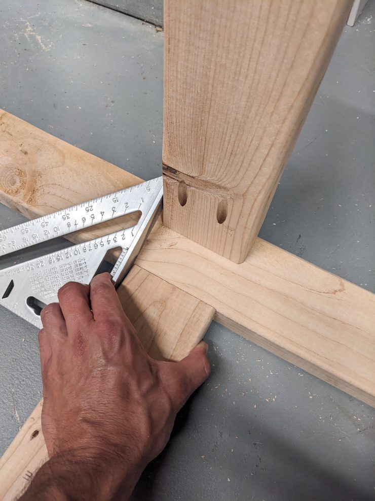 hand holding a speed square and pieces of wood
